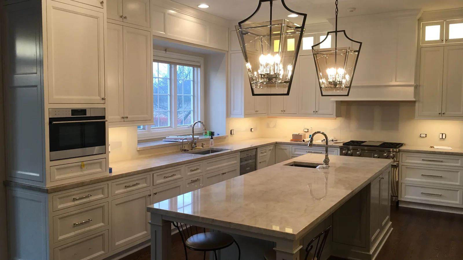 White kitchen cabinets with lantern pendants and a marble island