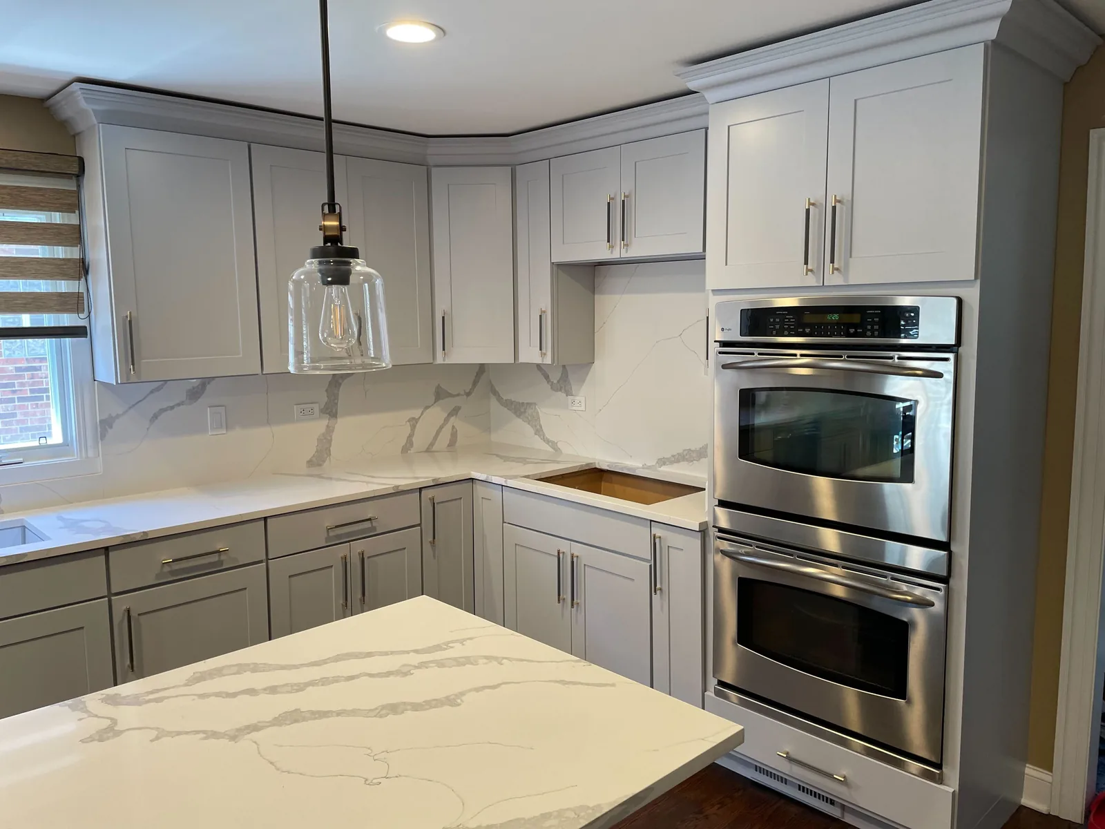 Gray refinished cabinets with a marble backsplash and double ovens