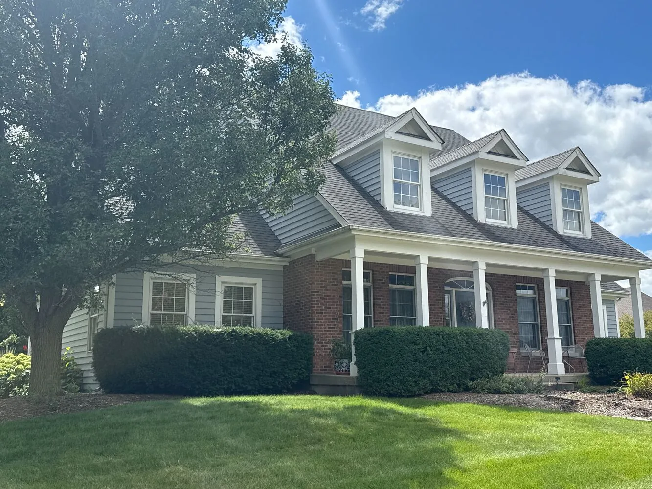 Gray Cape Cod with three dormers and a brick base after an exterior repaint