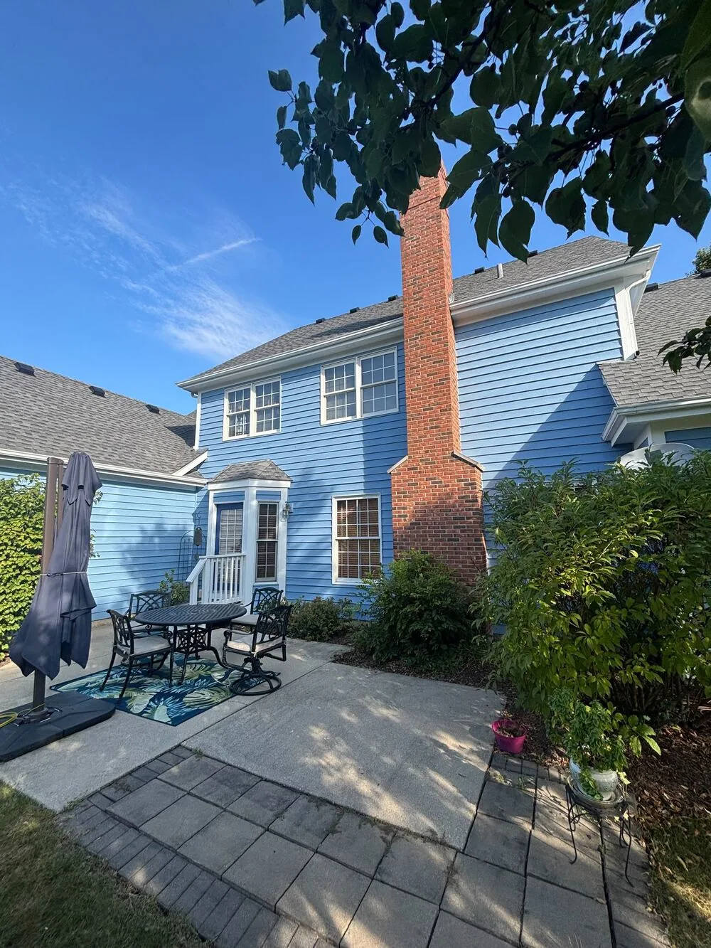 Light blue two story home with a brick chimney and a paver patio