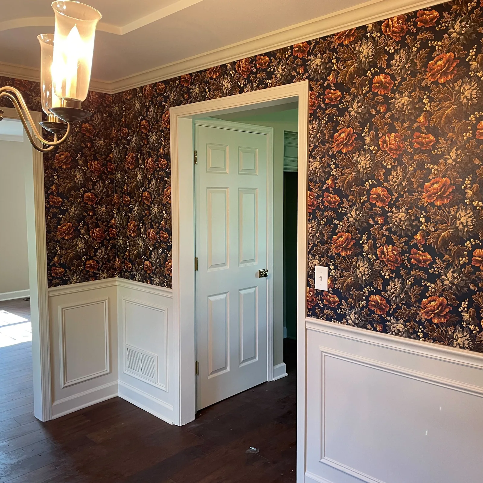 Dark floral wallpaper above white wainscoting